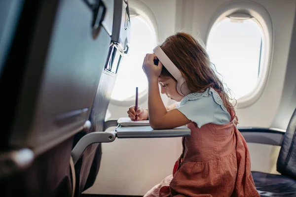 Little girl in an airplane drawing and listening music.