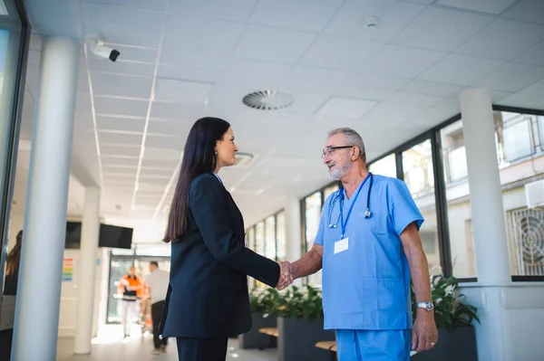 病院の部屋で若いビジネス女性が高齢者の医者と握手 — ストック写真
