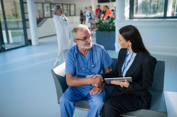 病院で高齢の医者と握手をする若いビジネス女性 — ストック写真