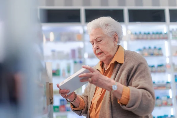 薬局に立って薬箱のテキストを読んでいるシニア女性 — ストック写真