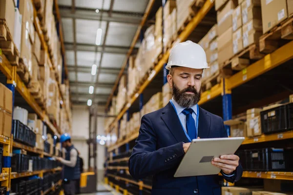 Manager in suit controlling goods in warehouse.