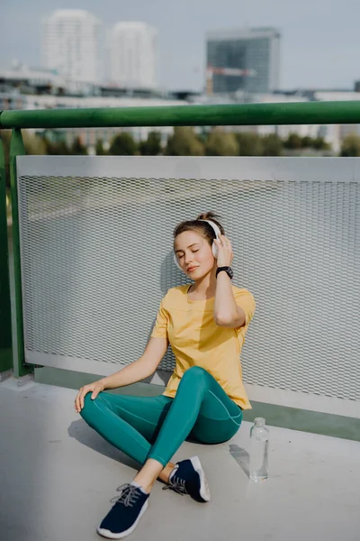 若い女性は 水を飲んで 音楽を聞くスルーヘッドフォン 市内でジョギング中 健康的なライフスタイルとスポーツの概念 — ストック写真