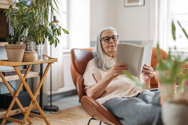 Старшая Женщина Читает Книгу Наслаждаясь Временем Одиночестве Своей Квартире — стоковое фото