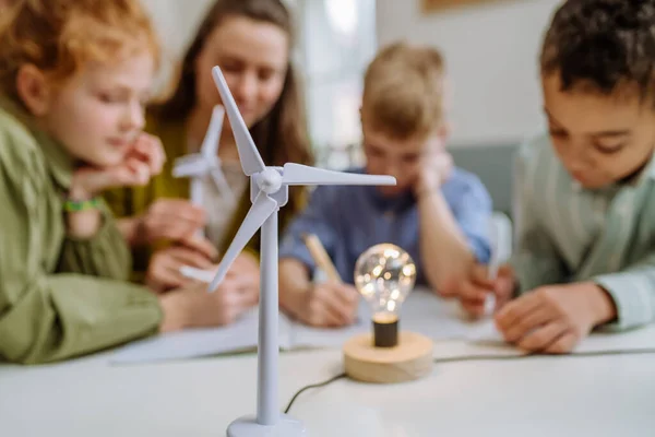 Young teacher with model of wind turbine learning her pupils about wind energy.