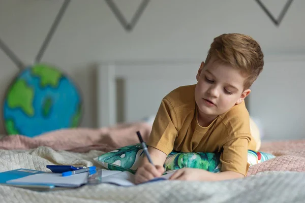 ベッドに横になって宿題をしている男の子 — ストック写真