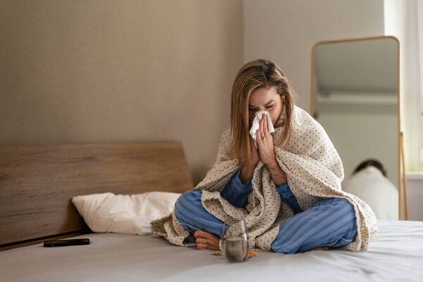 Sick woman sitting on a bed with a blanket.