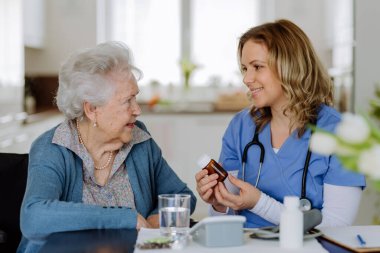 Nurse giving pills to senior woman in her home.