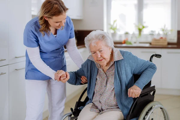 Nurse helping senior woman to stand up from a wheelchair.