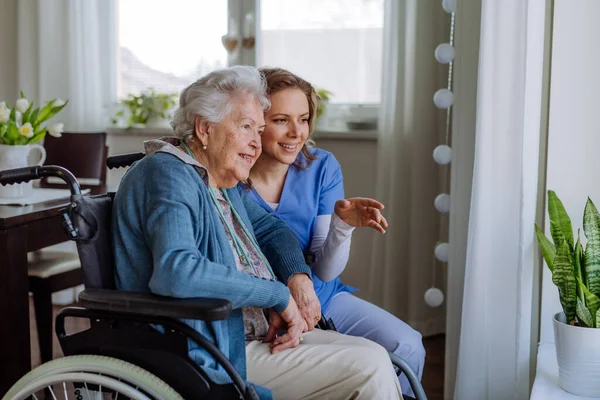 窓から外を見る車椅子の看護師と彼女のシニアクライアントの肖像画 — ストック写真