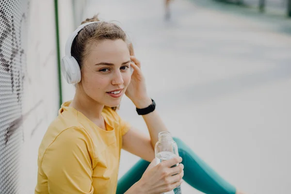 若い女性は 水を飲んで 音楽を聞くスルーヘッドフォン 市内でジョギング中 健康的なライフスタイルとスポーツの概念 — ストック写真