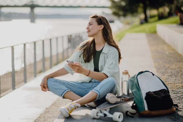 市内の公園に座ってスマホをスクロールする幸せな若い女性 若者文化と通勤概念 — ストック写真