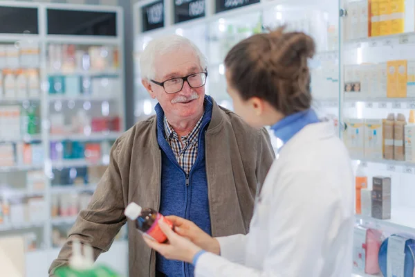 若い薬剤師は老人が薬を選ぶのを助ける — ストック写真