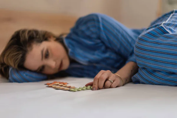 うつ病の若い女性がベッドに横たわって薬を見て — ストック写真