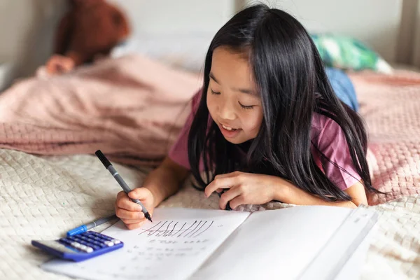 Küçük Kız Yatakta Uzanıyor Ödevlerini Yapıyor — Stok fotoğraf