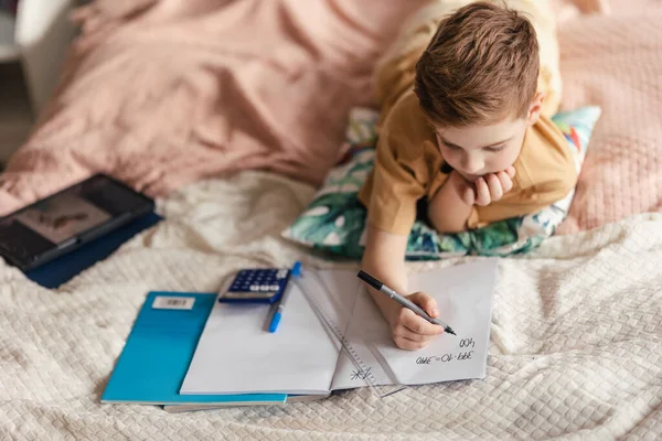 Küçük Çocuk Yatakta Uzanıyor Ödevini Yapıyor — Stok fotoğraf