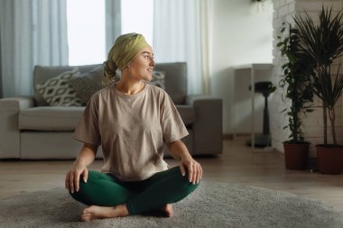 Kanserli genç bir kadın evde yoga yapıyor ve meditasyon yapıyor..