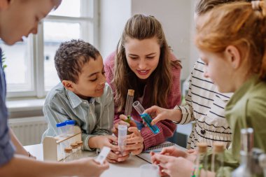 Genç öğretmen fen eğitimi sırasında öğrencileriyle kimya deneyi yapıyor..