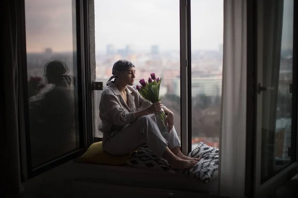 Młoda Kobieta Rakiem Siedząca Oknie Wąchająca Bukiet Tulipanów — Zdjęcie stockowe