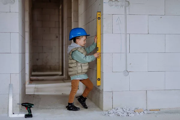 小男孩在未完工的房子里测量着未完工的房子的墙壁和精神水平 — 图库照片