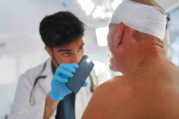 負傷した頭を持つシニア男を調べる医師 — ストック写真
