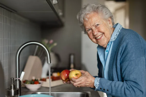 快乐的老年妇女在厨房里洗苹果 — 图库照片