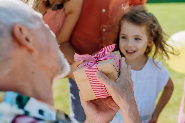 在夏日花园举行的世世代代家庭生日会上 一个快乐的小女孩送给她的祖父一份生日礼物 — 图库照片