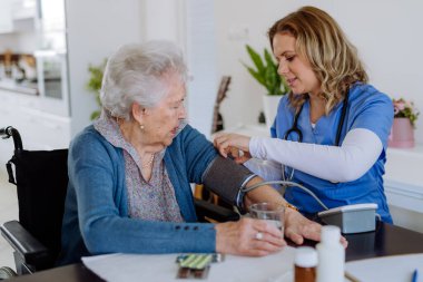 Nurse measuring blood pressuer to senior woman in her home.