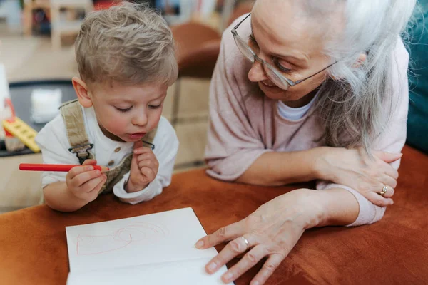 孫は祖母とノートパッドで絵を描く クレヨンで絵を描く男の子 — ストック写真