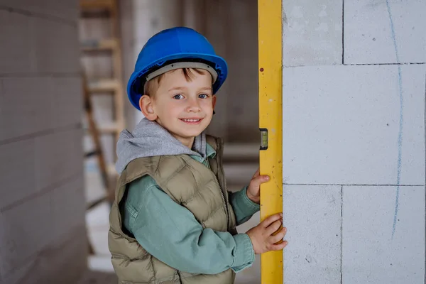 小男孩在未完工的房子里测量着未完工的房子的墙壁和精神水平 — 图库照片