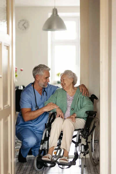 彼女の家で定期的にシニアクライアントのチェックアップを行う介護者 車椅子高齢者の看護をする男看護師 — ストック写真