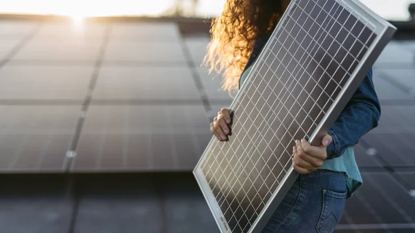 用光电电池板把一个拿着太阳能电池板的妇女关在屋顶上 — 图库照片