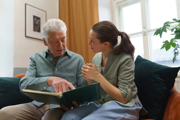 祖父和他的孙女在看家庭相册 怀旧的老人通过照片展示了他年轻时的照片 让人想起了过去的日子 — 图库照片
