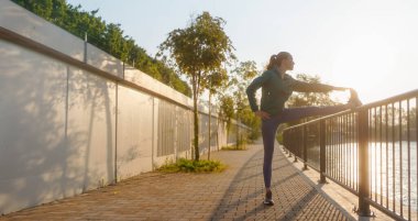 Spor giyimli genç bir bayan sabah koşusundan önce esneme egzersizleri yapıyor. Fitness kızı akşam egzersizi için hazırlanıyor. Açık hava idman konsepti.