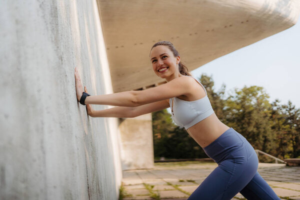 Portrait of young sporty woman in sportswear excercising outdoors. Fitness woman in front of concrete wall in the city. Healthy lifestyle concept. Street workout.