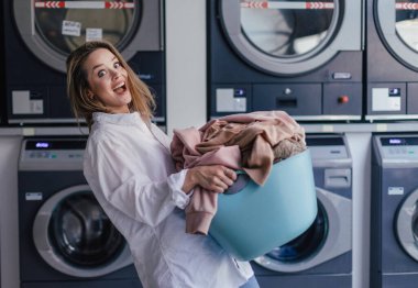 Young woman waiting in the laundry room. clipart