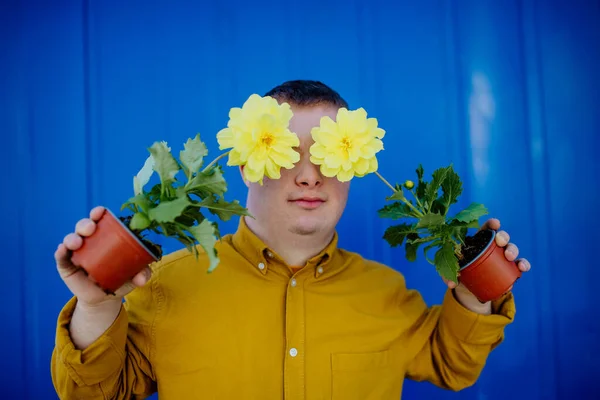 一个快乐的年轻人 患有唐氏综合征 笑容满面 拿着蓝色背景的盆花 — 图库照片
