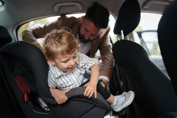 stock image Young father gvinig his little son in a car seat.