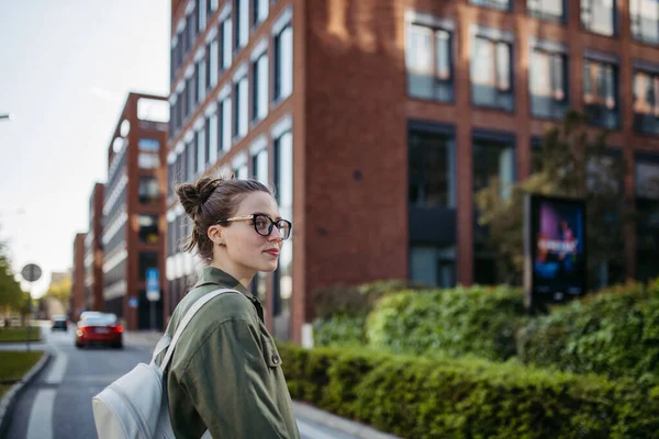 街の通りに眼鏡をかけた若い女性の肖像画 赤レンガ造りの建物の前に立って — ストック写真