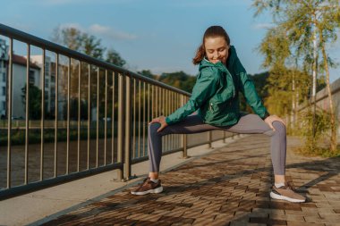 Genç bayan koşucu sabah koşusundan önce geriniyor. Spor giyim bölümündeki fitness kızı akşam egzersizi için hazırlanıyor. Açık hava idman konsepti.