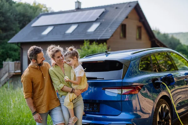 有一个家庭 他们的小女儿站在屋前 屋顶上有太阳能电池板 有电动汽车 — 图库照片