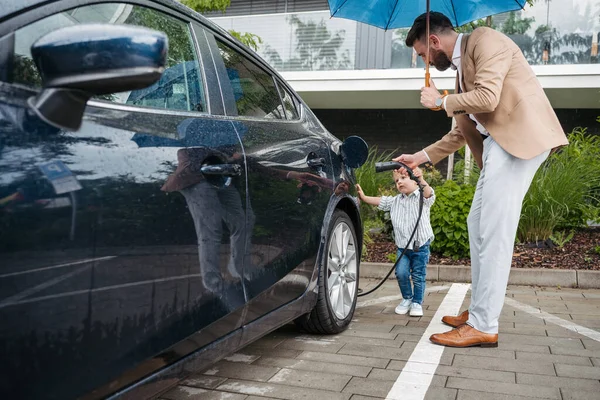 Mature Man His Little Son Charging Electric Car Rainy Day — Stock Photo, Image