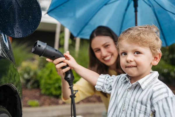 Usmívající Žena Její Malý Syn Nabíjejí Své Elektrické Auto Deštivém — Stock fotografie