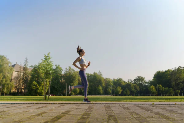 午前中に市内を走るアクティブウェアで運動選手の若い女性の側面図 アウトドアワークアウトのコンセプト コピースペース付きバナー — ストック写真