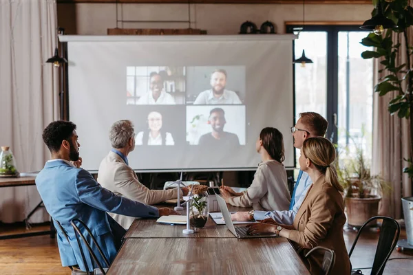 Employees having online business conference video call on wall display screen in board meeting room. Videoconference presentation, global virtual group corporate online meeting concept.