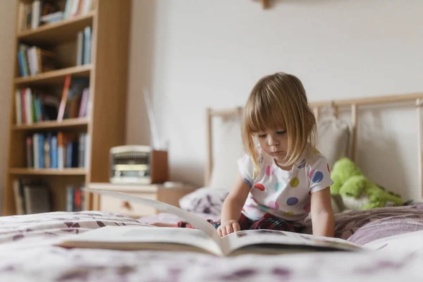 Cute Little Girl Grzywką Czytania Książki Leżącej Łóżku Pokoju Dzieci — Zdjęcie stockowe