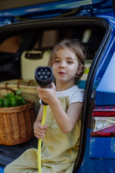 Küçük Kız Elinde Güç Kaynağı Kablosu Arabanın Bagajında Oturuyor — Stok fotoğraf