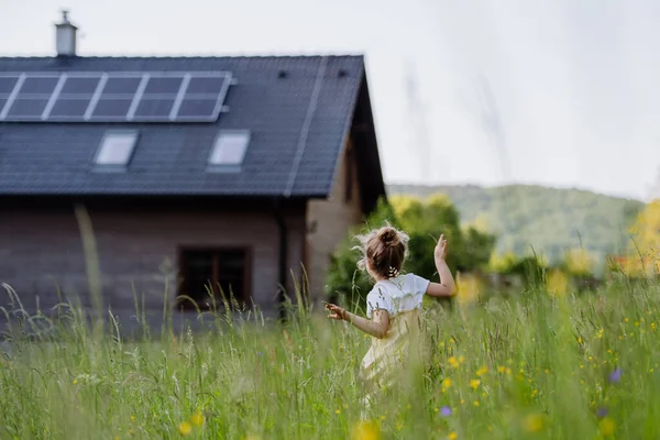 stock image Rear view of a little girl in front of family house with solar panels, concept of sustainable lifestyle and renewable resources.