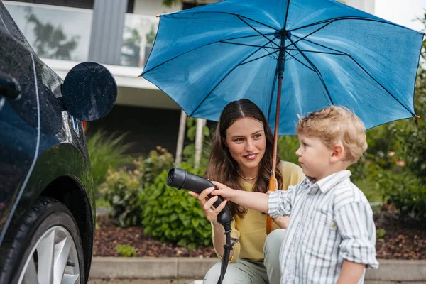 Smiling Woman Her Little Son Charging Electric Car Rainy Day — Stock Photo, Image