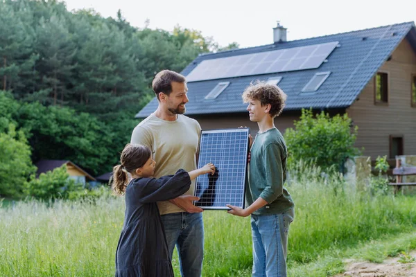 屋根の上に太陽光発電で家の前に立っている父と彼の子供 — ストック写真