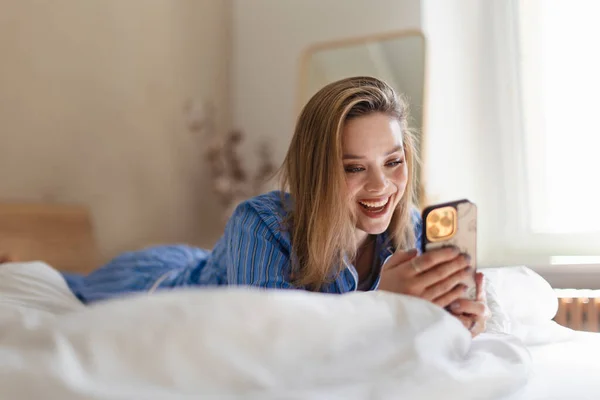 Genç Bir Kadın Yatağında Uzanıyor Akıllı Telefonu Kaydırıyor — Stok fotoğraf